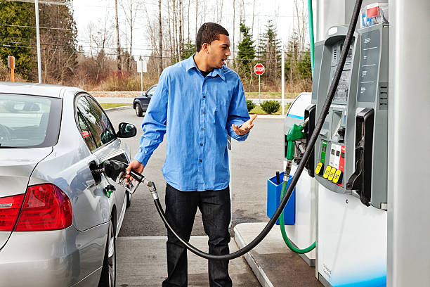 "Photo of a young man watching filling his gas tank, watching in disbelief as the dollar amount climbs on the gas pump display too quickly to comprehend."