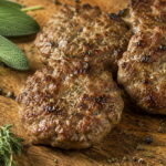 Breakfast Sausage Seasoning: Every Question Answered Close-up of homemade breakfast sausage patties with fresh sage, black pepper, and dried thyme on a wooden cutting board