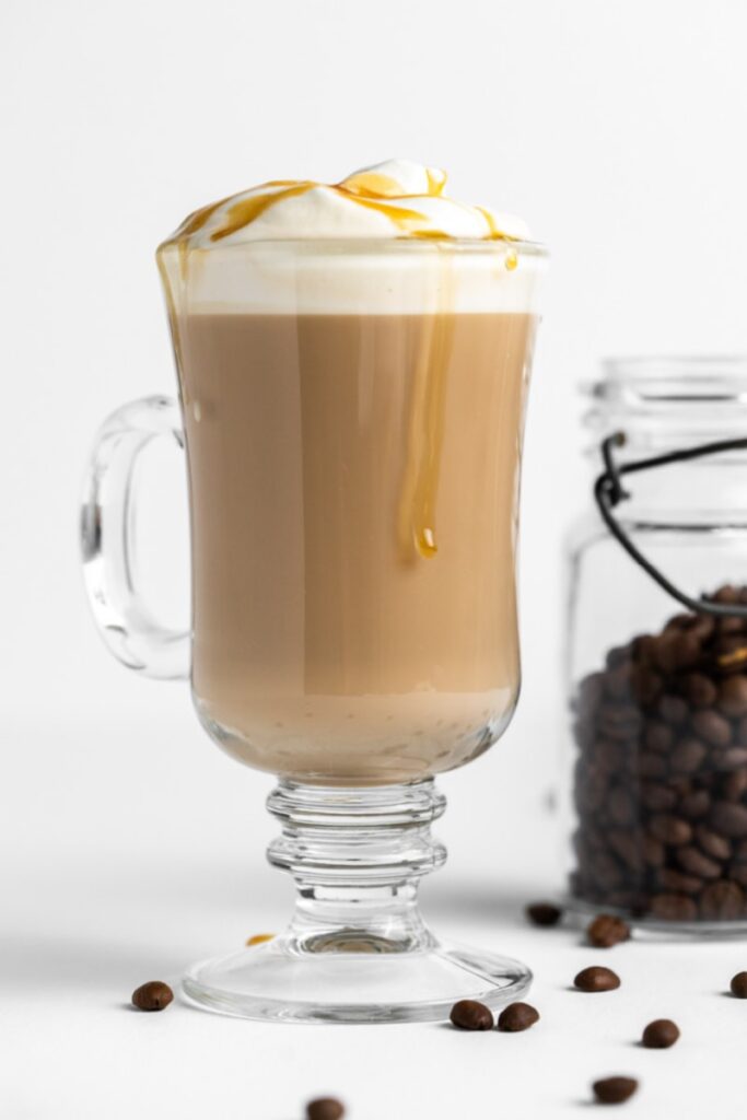 Hot caramel macchiato with whipped cream and caramel drizzle in a glass mug