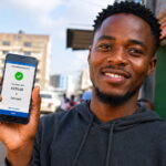How to Repay Zamcash Loans in Zambia (Step-by-Step Guide) Young Zambian man smiling while using an Android smartphone showing a Zamcash loan repayment confirmation via Airtel Money outdoors in Zambia