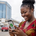 Instant Mobile Money Loans in Zambia Without Collateral Young Zambian woman smiling at a successful mobile money transaction on her smartphone in Lusaka city street - Instant Mobile Money Loans in Zambia Without Collateral