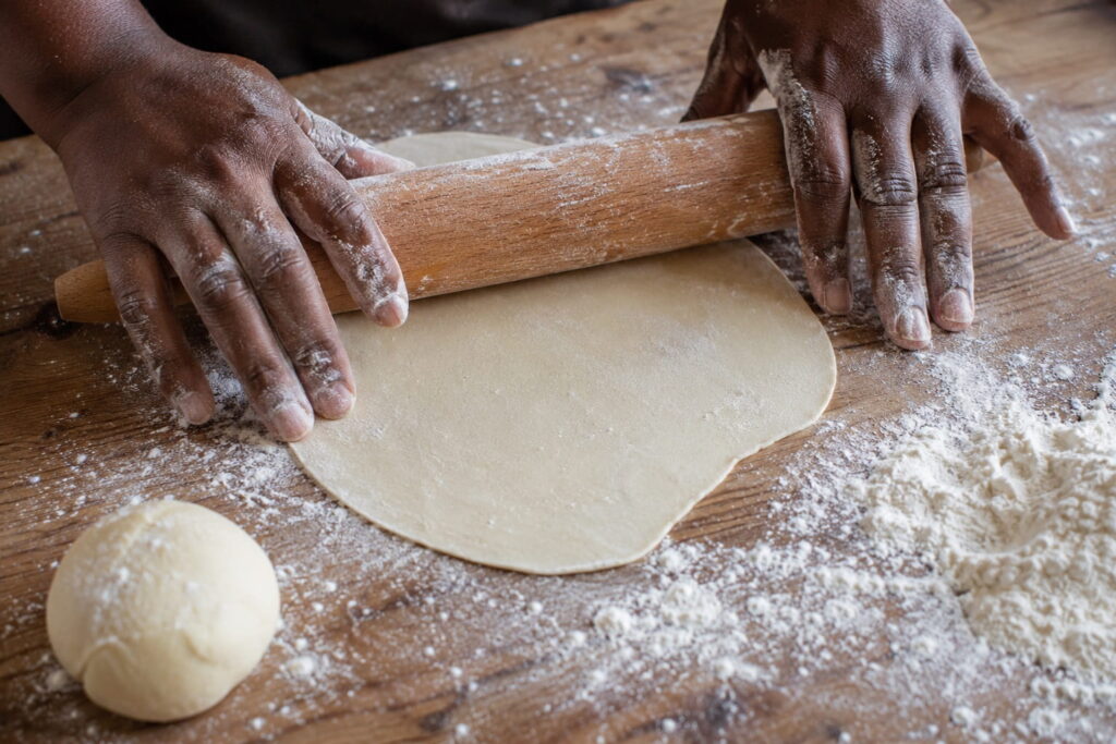 Hands rolling out samosa dough on a floured wooden surface