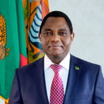 Official portrait of President Hakainde Hichilema of Zambia standing before the national flag - Zambia Elections Winner 2026