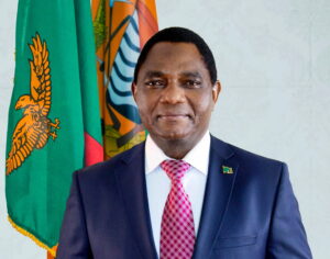 Official portrait of President Hakainde Hichilema of Zambia standing before the national flag - Zambia Elections Winner 2026